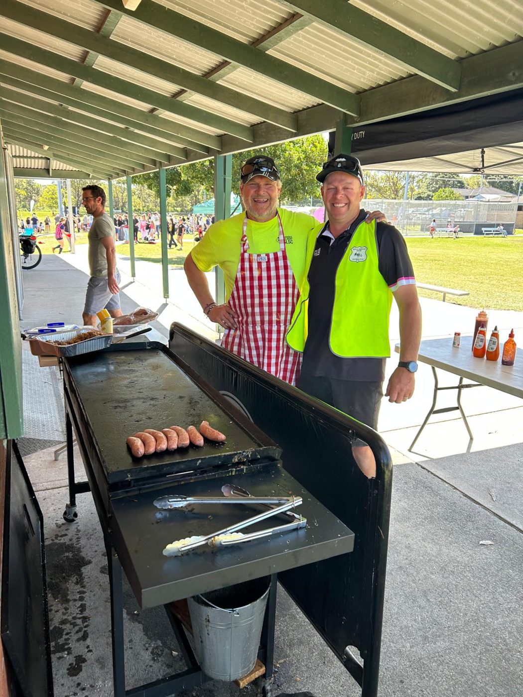 Two Dudley Redhead United volunteers cooking sausages on the club BBQ at a busy community event